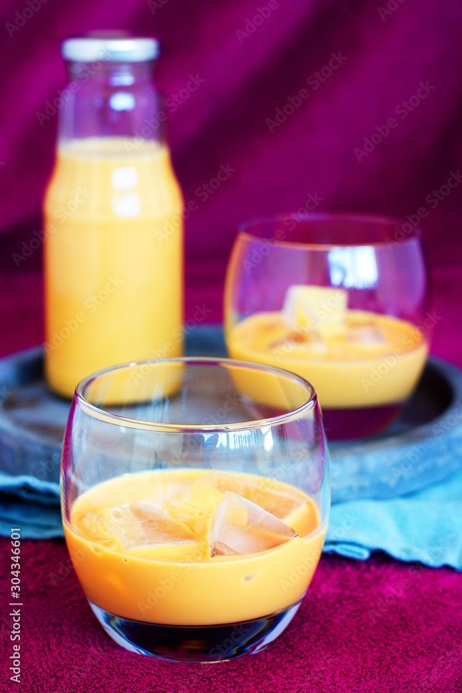 Homemade caramel alcohol drink served in pure glass with ice cubes on concrete tray and blue cloth with purple background Homemade caramel alcohol drink served in pure glass with ice cubes on concrete tray and blue cloth with purple background