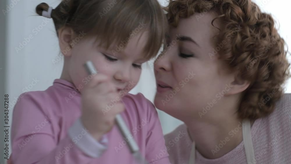 Parent plays with the child in the cook. Mom kisses her daughter while cooking. The child kneads the dough in the kitchen under the supervision of mom. Parent plays with the child in the cook. Mom kisses her daughter while cooking. The child kneads the dough in the kitchen under the supervision of mom.