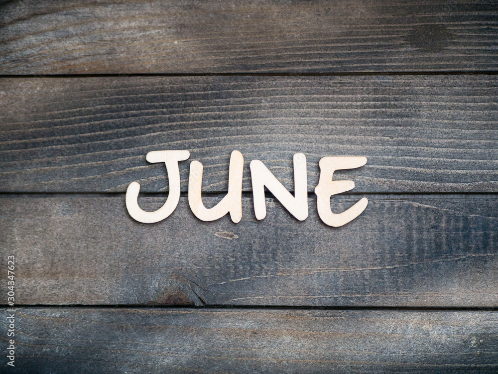 Fototapeta premium The name of the month is composed of light wooden letters on dark wood. The month of June.