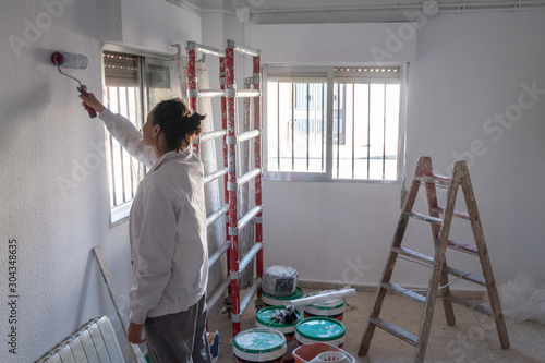 Young woman painting interior wall with white paint. .paint cans and painter ladder.