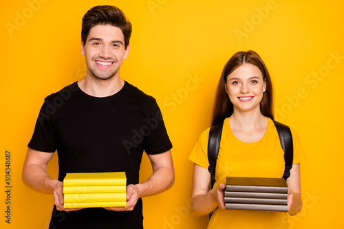 Photo of cheerful positive cute clever nice groupmates holding tutorials in their hands wearing black t-shirt smiling toothily isolated over vibrant shine yellow color background photo