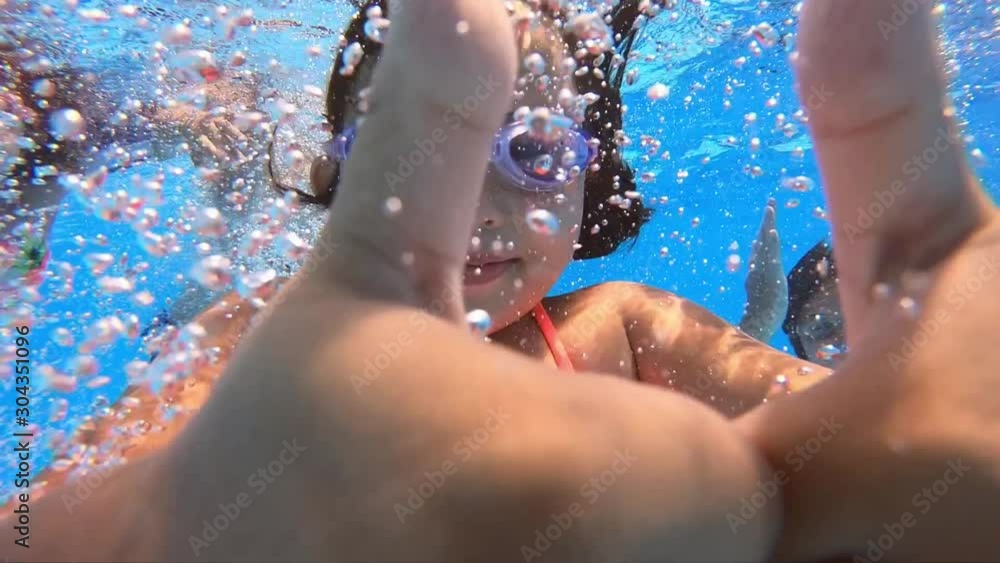 Underwater view of having fun group of children jumping and diving into swimming pool at pool party in summer sunny day. Happy children. Slow motion. Childhood, friendship, vacation concept