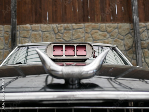 carburetor air intake with red flaps. Bull horns made of silver-colored metal on the hood of a black car. The decoration of the car in the Texas style.