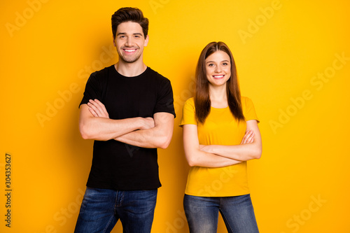 Photo of cheerful cute pretty nice couple with hands folded wearing jeans denim black t-shirt coworking standing confidently isolated over vivid yellow color background photo