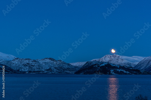 the lunar eclipse during blou hours above mountains lofoten norway. long shutter speed