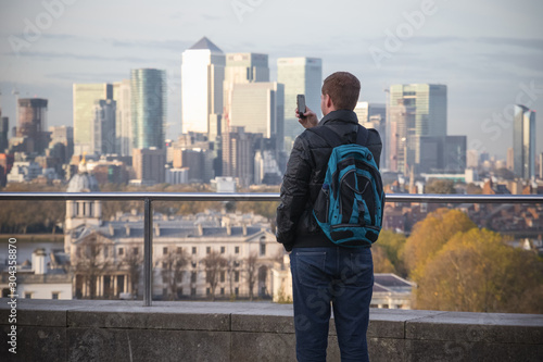 Back view of a male tourist taking pictures of London cityscape from Greenwich hill