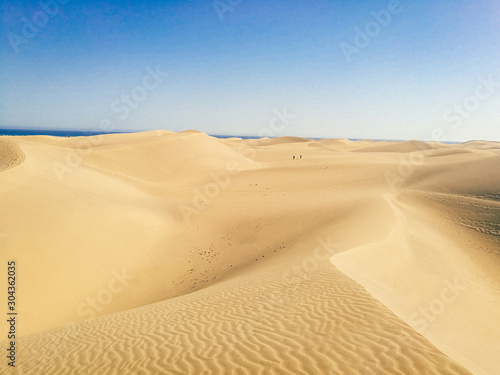 Fototapeta Naklejka Na Ścianę i Meble -  Wide landscape view of vast smooth sand dunes in Maspalomas, Las Palmas of Gran canaria, tropical Canary island in Atlantic ocean, Spain, people in distance