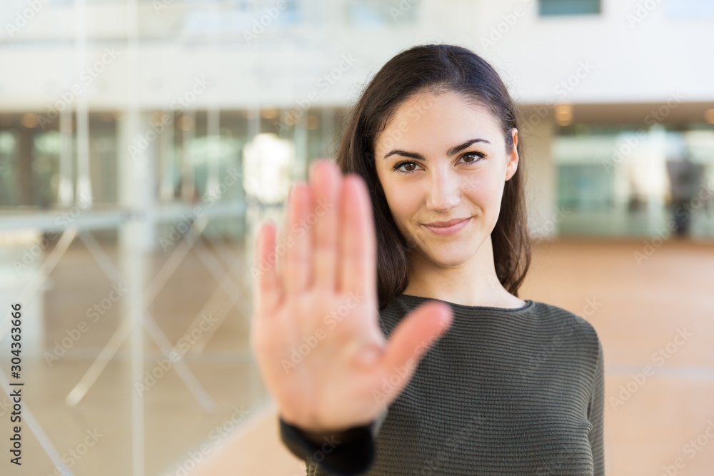 Friendly confident beautiful woman making hand stop gesture. Young woman in casual posing indoors with glass wall interior in background. Warning concept