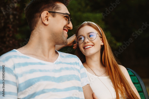 Close up of a charming young couple having fun laughing while sitting on a bench and looking to each other.