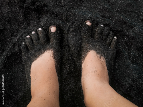 Young woman's feet covered in black sand on beach Playa de Guayedra in Las Palmas on Gran Canaria volcanic island, Spain, Atlantic, volcanic sand photo