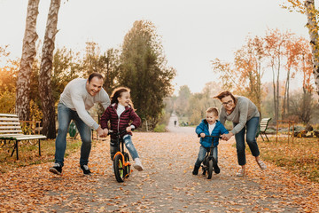 Lovely family playing with their kids while teaching them how to ride bicycles in the park.