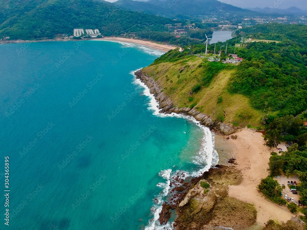 Wind turbine  Panorama drone aerial view electricity windmill overlooking Naiharn beach phuket Thailand turquoise blue waters white golden sandy beach lush green mountains 