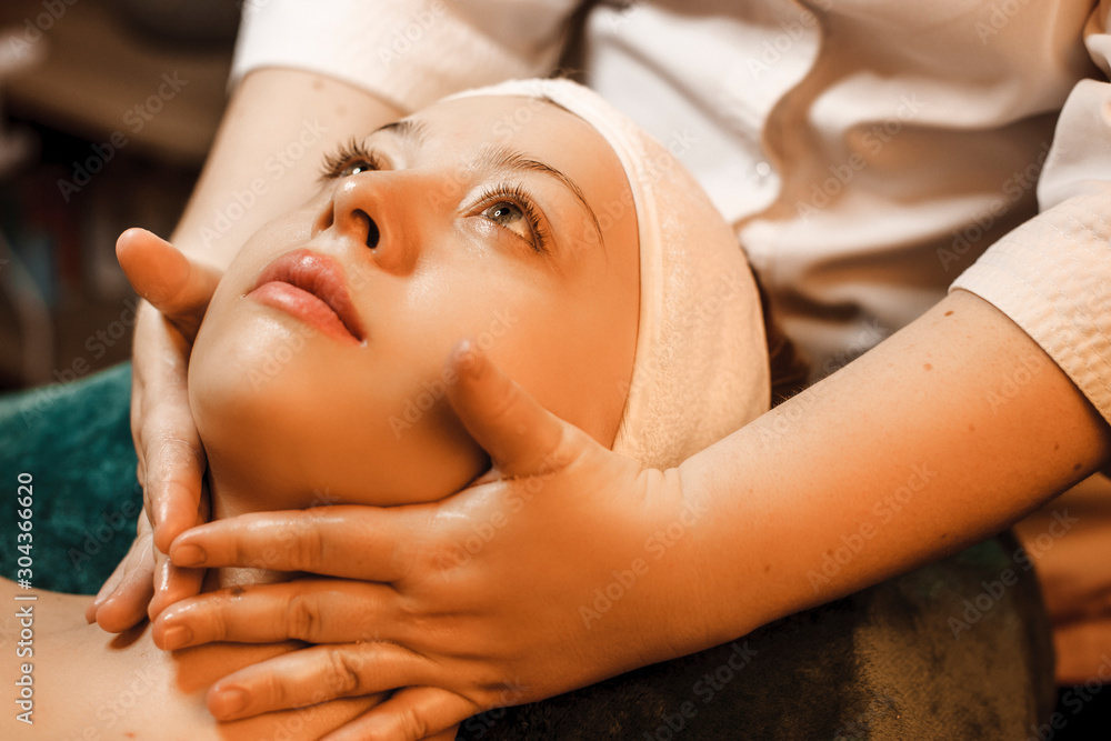 Close up of a young lovely woman relaxing while having a facial massage in a wellness spa center.