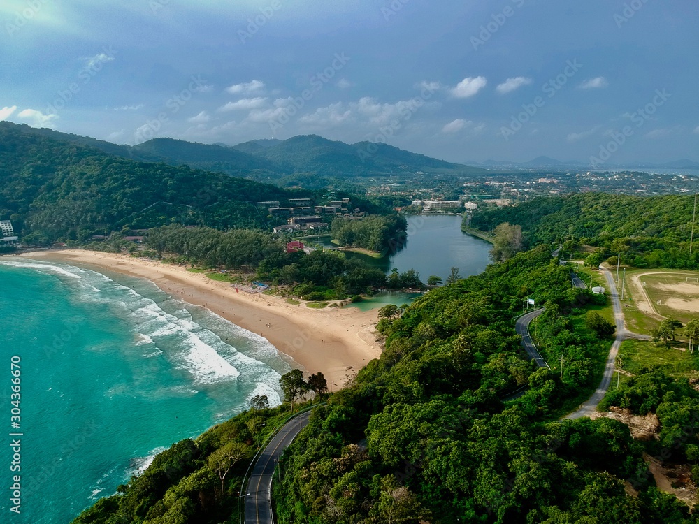 Panorama drone aerial view electricity windmill overlooking Naiharn beach phuket Thailand turquoise blue waters white golden sandy beach lush green mountains 