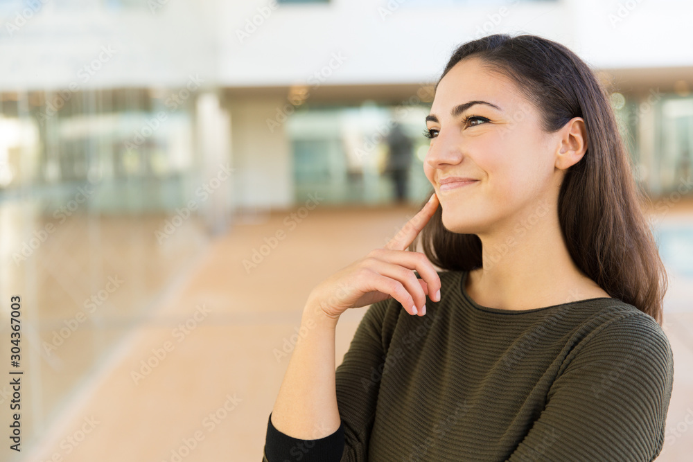 Joyful positive beautiful woman standing in hallway and looking at copy space away. Young woman in casual posing indoors with glass wall interior in background. Advertising concept Joyful positive beautiful woman standing in hallway and looking at copy space away. Young woman in casual posing indoors with glass wall interior in background. Advertising concept