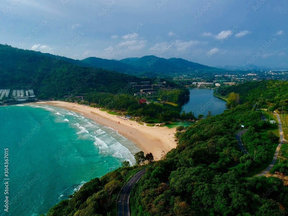 Panorama drone aerial view electricity windmill overlooking Naiharn beach phuket Thailand turquoise blue waters white golden sandy beach lush green mountains 
