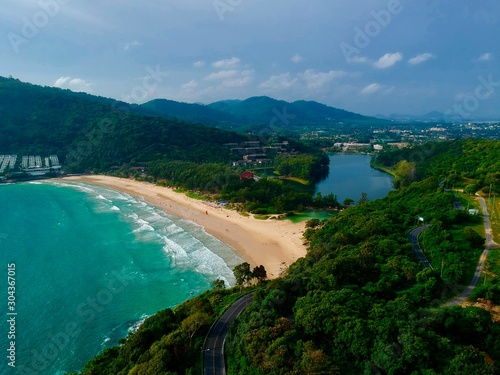 Panorama drone aerial view electricity windmill overlooking Naiharn beach phuket Thailand turquoise blue waters white golden sandy beach lush green mountains 