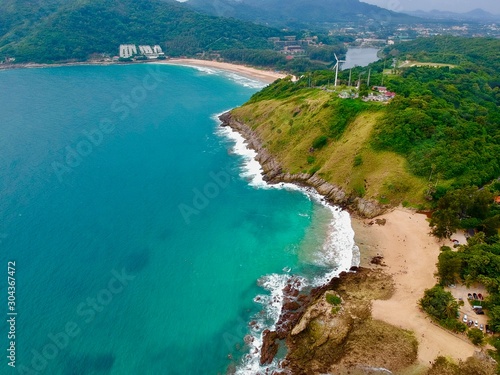 Wind turbine Panorama drone aerial view electricity windmill overlooking Naiharn beach phuket Thailand turquoise blue waters white golden sandy beach lush green mountains 