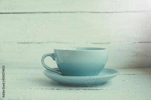 Blue cup and saucer on a white wooden background side view.