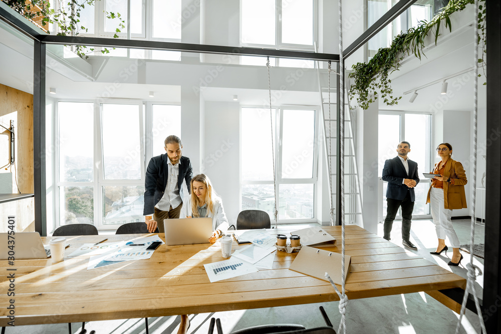 Office employees talking and having some office work at the large meeting table, wide view on the spacious room with large windows