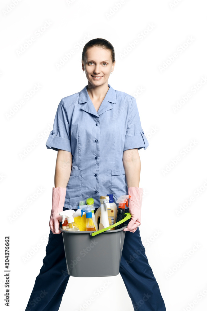 Attractive young woman in cleaning uniform and rubber gloves holding a bucket of cleaning products in her hands, isolated on white background Attractive young woman in cleaning uniform and rubber gloves holding a bucket of cleaning products in her hands, isolated on white background