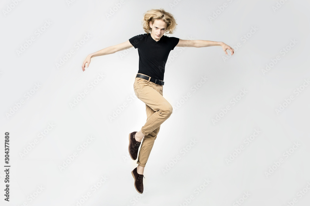 A frantic and expressive jump, hair scatter in different directions. Portrait of a jumping man on a light background.