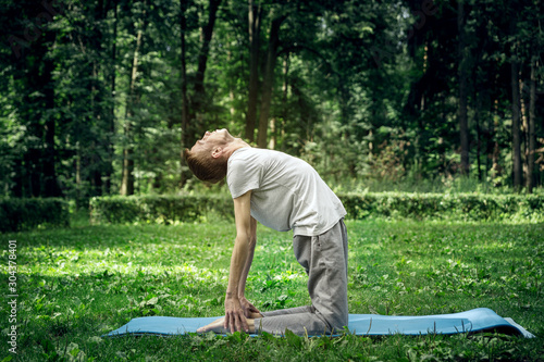 A young man in sportswear is doing yoga in the park. Does the exercise bend backwards in the back.