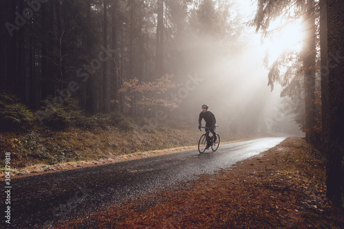 Rennradfahrer im Wald bei herbstlichem Wetter mit Sonnenstrahlen im Nebel