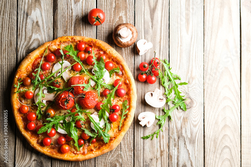 Traditional italian pizza with tomatoes, cheese, ham, mushrooms and arugula on a light rustic background top view copy space. . photo