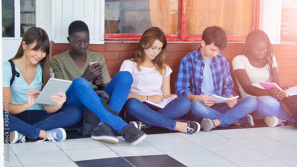 Multi ethnic schoolmates sitting in the school hallway relaxing and doing school lesson Multi ethnic schoolmates sitting in the school hallway relaxing and doing school lesson