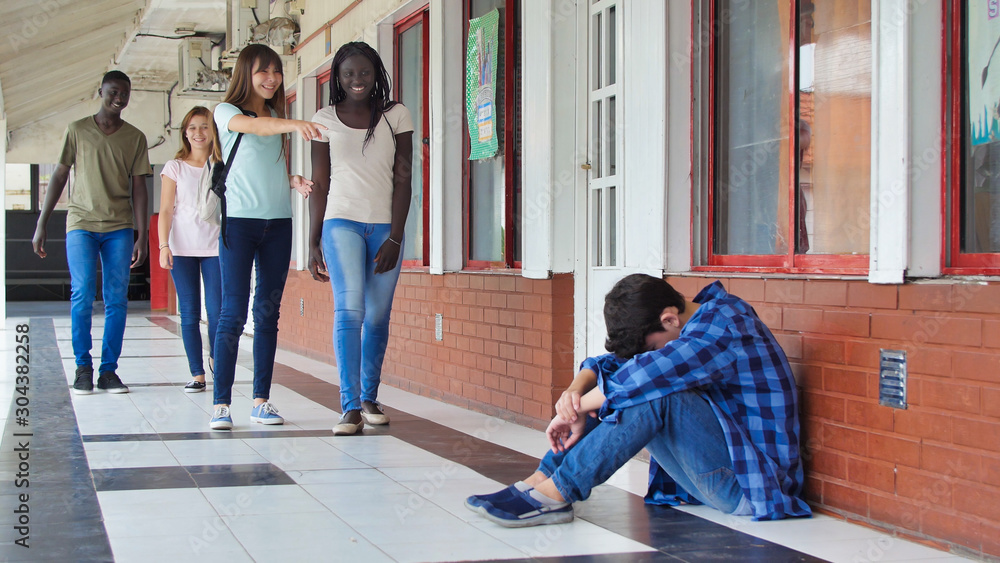 Young caucasian sitting alone with sad feeling at school. Child in depression abandoned in a corridor and leaning against brick wall. Bullying, discrimination and racism concept Young caucasian sitting alone with sad feeling at school. Child in depression abandoned in a corridor and leaning against brick wall. Bullying, discrimination and racism concept