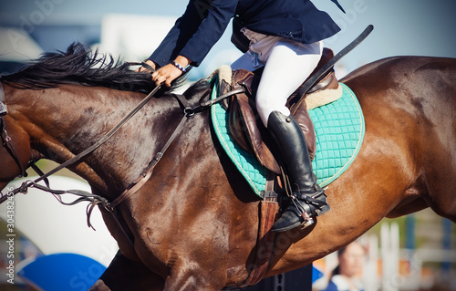 A rider on sits astride a horse in the saddle while the horse is in a jump over a barrier at an equestrian show jumping competition.