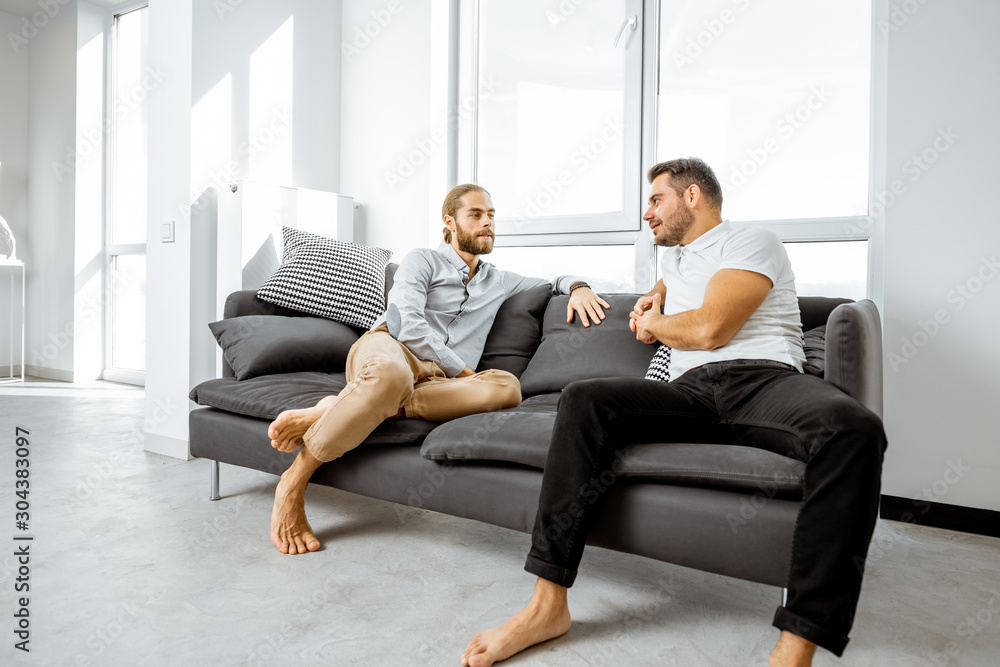Two male friends having a serious discussion while sitting together on the couch in the living room at home