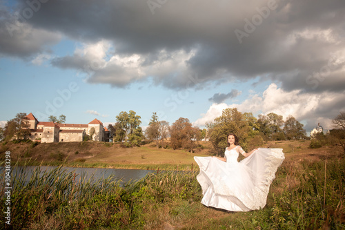 fairy-tale princess in light dress on wide path and walks towards wind. Beautiful bride in a white dress with long train