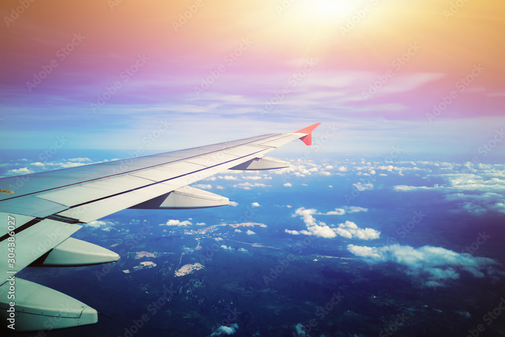 Obraz premium Airplane wing with sunrise in light flare by looking through the airplane window. - Image