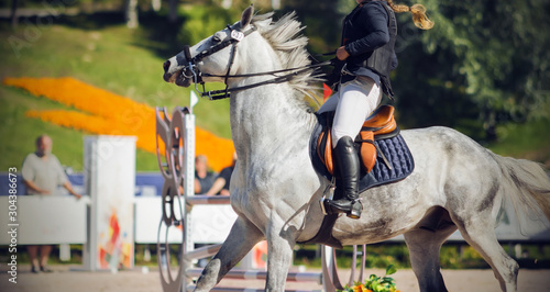 The girl rider sits in the saddle on a fast galloping gray horse and which performs at competitions on show jumping