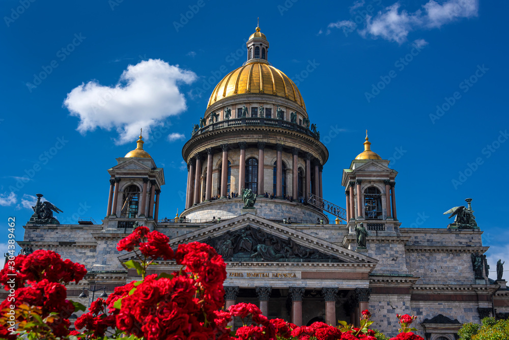 Russia, Saint Petersburg: Golden dome of famous Saint Isaac's Cathedral or Isaakievskiy Sobor with sculptures and columns in the city center of the Russian town with red roses flowers and blue sky.