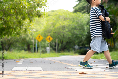 Фотография A little child, kindergarten boy hold his backpack walking on pedestrian crossing to school by himself