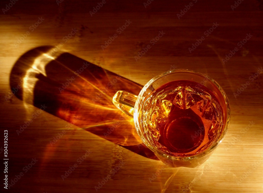 Top view photo of a glass cup of tea on a bamboo board, with beautiful shadows and reflections from sunlight. 