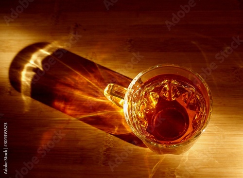 Top view photo of a glass cup of tea on a bamboo board, with beautiful shadows and reflections from sunlight. 