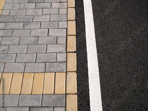 Top view photo of a fragment of a sidewalk paved with grey and yellow tiles and a bicycle lane with rubber coating.