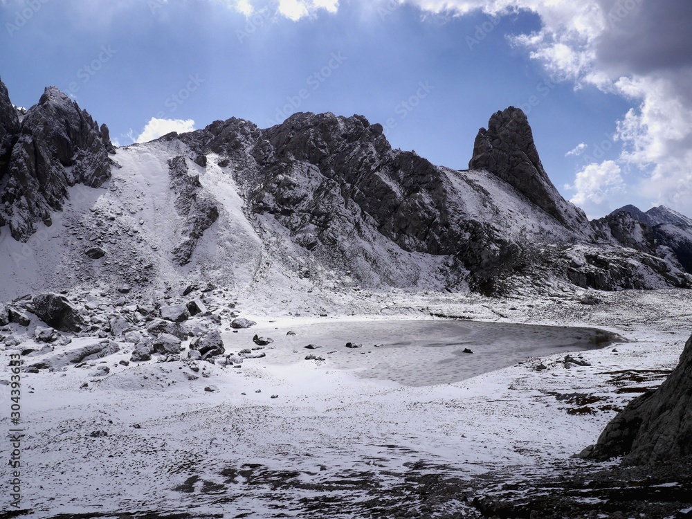 Photo of a mountain lake covered with snow and ice, on a sunny day.