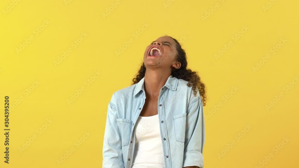 Young happy African American woman laughing loud and shouting against yellow background Young happy African American woman laughing loud and shouting against yellow background