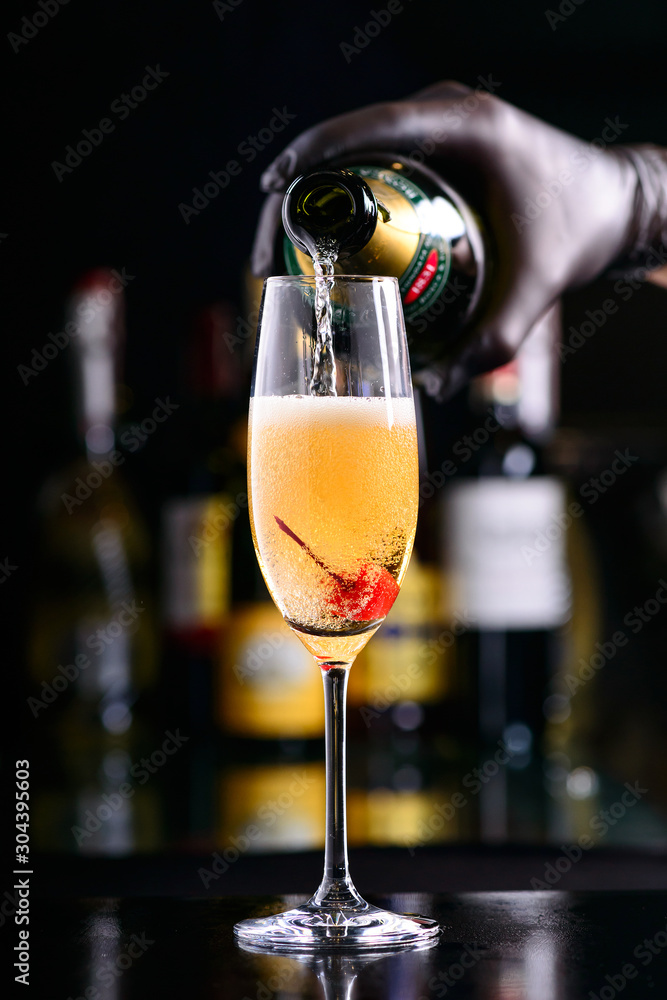 Fototapeta premium bartender pours bellini champagne cocktail into a glass with cherry