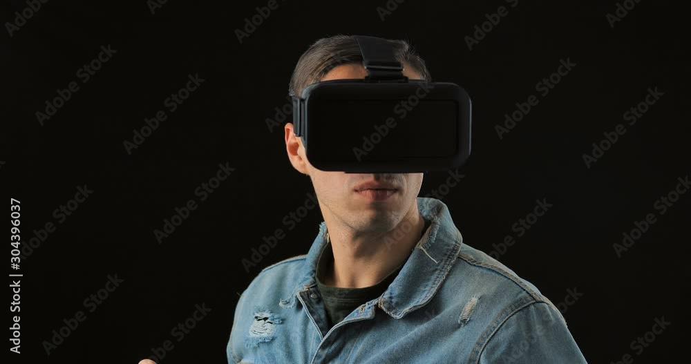 Young male wearing virtual reality technology VR Glasses. Man surprised by augmented reality in virtual reality helmet on a black background Young male wearing virtual reality technology VR Glasses. Man surprised by augmented reality in virtual reality helmet on a black background