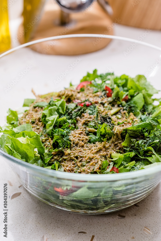 Homemade Salad with Herbal Sauce and Red Pepper Slices Mixed with Two Spoon in Glass Bowl.