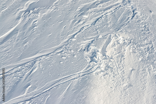 Snowy abstract off-piste skiing backround texture with ski and snowboard trails and tracks on new virgin powder snow. morning sunrise or evening sunset time at alpine mountain resort