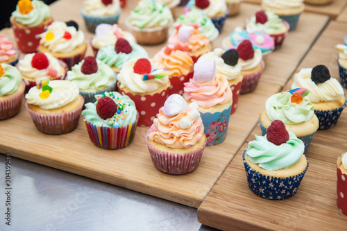 Assorted colorful cupcakes with blue, pink and orange frosting, decorated with raspberries, marshmallow, sprinkles and candies. 
