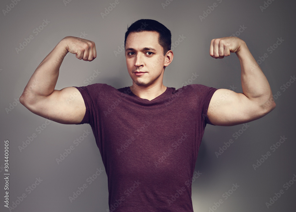 Naklejka premium Young casual strong man showing biceps on the arms on grey background. Closeup
