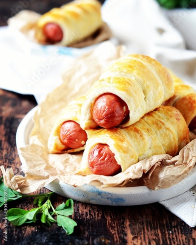 Sausages in the dough on a plate on a dark wooden table